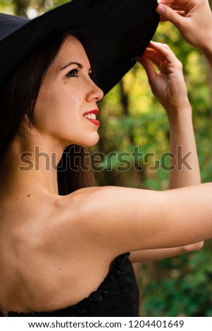 Halloween holiday background. Halloween Witch in a dark forest. Beautiful young woman in witches hat and costume.