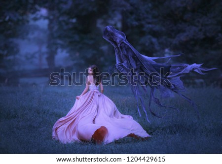 Beautiful girl in a long, pink, fluttering dress runs away from death in the form of a dark demon who came out of hell. Frightened brunette girl looks around. Artistic, gothic photo in cold colors
