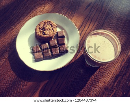 Chocolate milk in a glass. Chocolate pieces and chocolate cookies on a plate. Shadows from the plate and glass are clearly visible. The wood has a brown color. This picture shows an upper view.