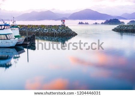 seascape sitka alaska, waterfront reflected sunrise colors on water. a coastal village with fishing and cruise vessels, mountains and sea smoke in background