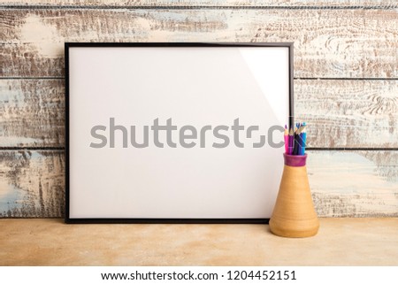 Mock up of an empty frame poster on a wall of wooden boards. Color pencils in a vase. Copy space  