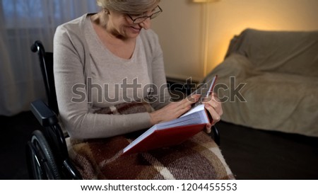 Lady in wheelchair looking at photos in album and smiling, good memories