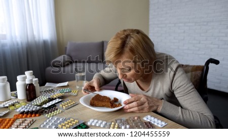 Sick disabled lady trying to eat dessert at table with pills, rehabilitation