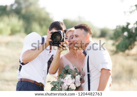 wedding photographer takes pictures of bride and groom in nature. photographer shows just taken photos to wedding couple