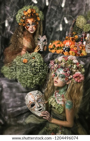 close up portrait of two young beautiful girls with flower professional makeup. elfs with flower crown on head. bright face art. fairies in Halloween decoration with pumpkins and candles. mask on hand