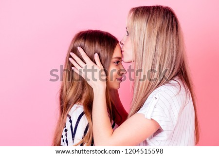 beautiful woman kisses her cute daughter on the forehead on a pink background in the studio. concept of family well-being and love