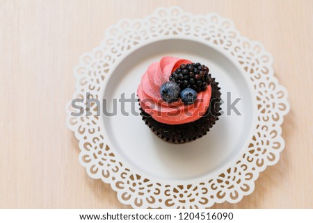 Chocolate cupcake with pink cream and berries served on white lace decorated plate