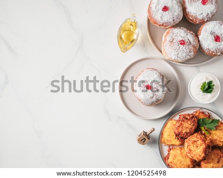 Jewish holiday Hanukkah concept and background. Hanukkah food doughnuts and potatoes pancakes latkes, oil and traditional spinnig dreidl. on marble table. Top view or flat lay. Copy space for text.