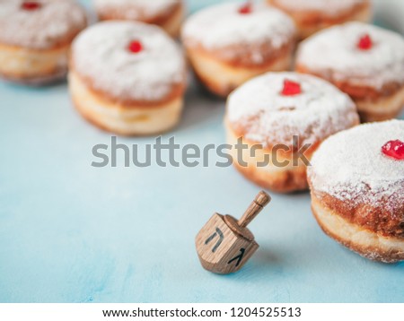 Jewish holiday Hanukkah concept and background. Hanukkah food doughnuts and traditional spinnig dreidl or dredel on blue background. Copy space for text. Shallow DOF