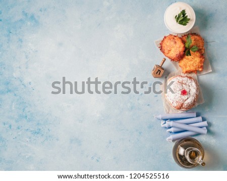 Jewish holiday Hanukkah concept and background. Hanukkah food doughnuts and potatoes pancakes latkes, oil and traditional spinnig dreidl on blue background. Top view or flat lay. Copy space for text.