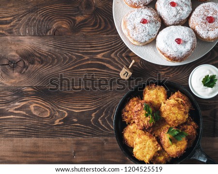 Jewish holiday Hanukkah concept and background. Hanukkah food doughnuts and potatoes pancakes latkes, oil and traditional spinnig dreidl on wooden table. Top view or flat lay. Copy space for text.