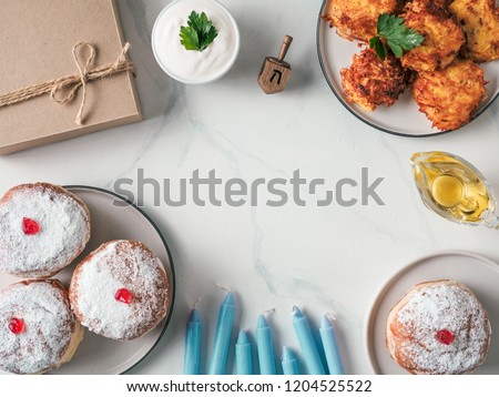 Jewish holiday Hanukkah concept and background. Hanukkah food doughnuts and potatoes pancakes latkes, oil, candles, gift box and traditional spinnig dreidl. Top view or flat lay. Copy space for text