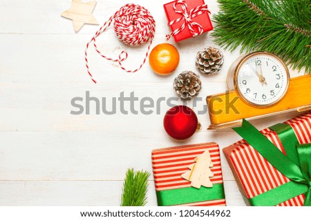 New Year or Christmas background. Retro alarm clock pine branches cones gifts presents toys red ball on white wooden background top view with copy space. Christmas timer Time to celebrate Xmas