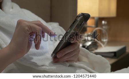 Closeup of young woman hands typing sms scrolling phone pictures. female hands use a smartphone in the evening on the bed.