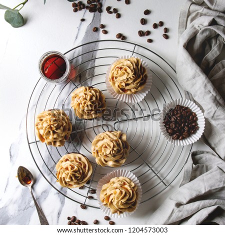 Fresh baked homemade cupcakes with coffee buttercream and caramel standing on cooling rack with eucalyptus branch and coffee beans above over white marble background. Flat lay. Square image