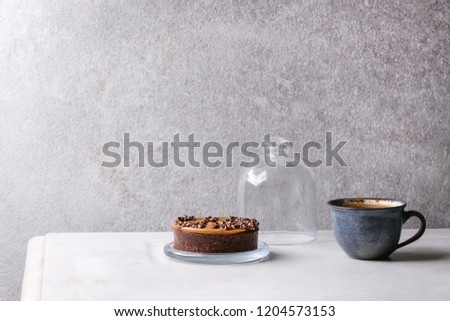 Sweet chocolate tartlet with cup of coffee espresso standing on white marble table with grey wall at background. Minimalist style. Copy space
