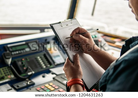 Marine navigational officer or chief mate on navigation watch on ship or vessel. He fills up checklist. Ship routine paperwork Royalty-Free Stock Photo #1204631263
