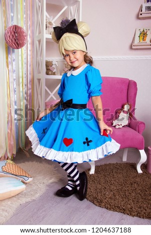 little girl in blue dress. kid halloween costume. young happy girl in white room is standing in pink armchair and flirting with beauty smile near gifts