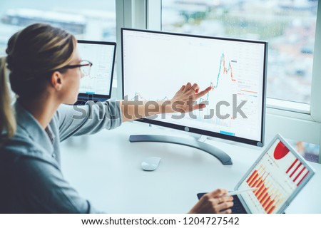 Business woman study financial market to calculate possible risks and profits.Female economist accounting money with statistics graphs pointing on screen of computer at desktop. Quotations on exchange Royalty-Free Stock Photo #1204727542