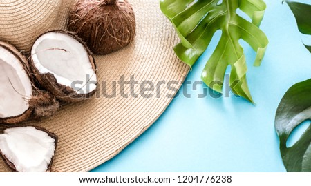 colorful summer with coconuts and a beach hat on a blue background with real tropical leaves, summer fashion