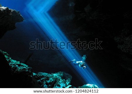 Scuba diver swimming underwater in the sun beams. Large cenote cave with blue light rays and scuba diver. 