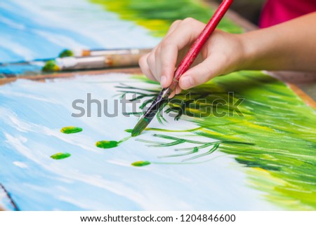 Child paints a picture by gouache. Kid drawing at white paper. The hand and paint brush. Closeup, selective focus