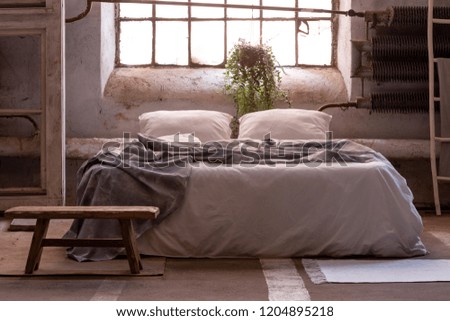 Real photo of a wabi sabi bedroom interior with a bed, plant and wooden stool in front