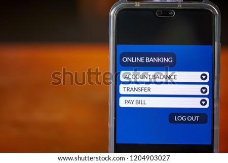 Online banking concept. Smartphone screen display mobile banking app for financial transaction with wooden table background. Front view & close up. All screen graphics are made up with own design.