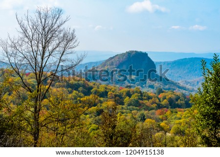 Beautiful autumn fall foliage colors against blue skies with puffy colors. Hills and mountain range in background.