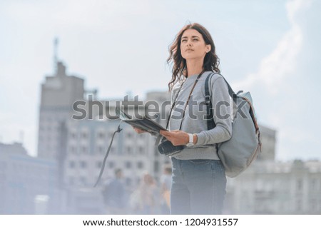 attractive female tourist with photo camera, backpack and map walking in city