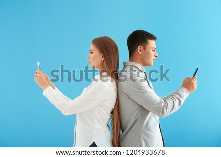 Young couple with mobile phones on color background