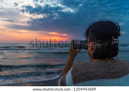 Girl takes pictures on smartphone dawn on the sea