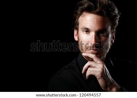 Closeup portrait of confident man thinking, wearing black, looking at camera, black background.