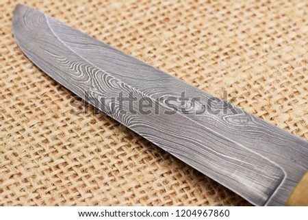 Traditional handmade Finnish knife with the abstract wave pattern of damascus steel over an old sack background. 