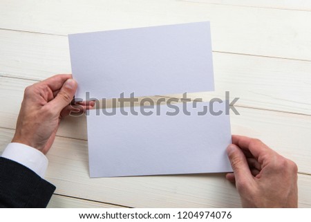 Mens hands holding empty white flyers on wooden background