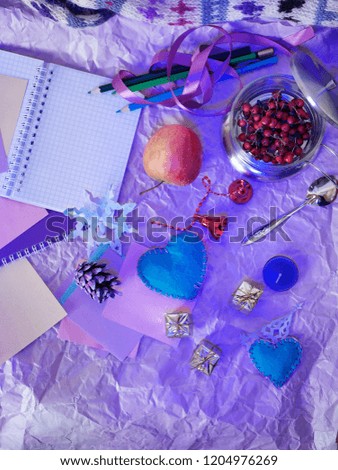 Seasonal decorative Christmas composition from a notebook, pencils, felt hearts, cut out of paper, snowflakes and figures of angels, cones, golden gifts, Christmas decorations on a light background
