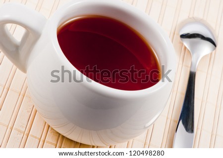 White cup with fresh tea on wooden mat