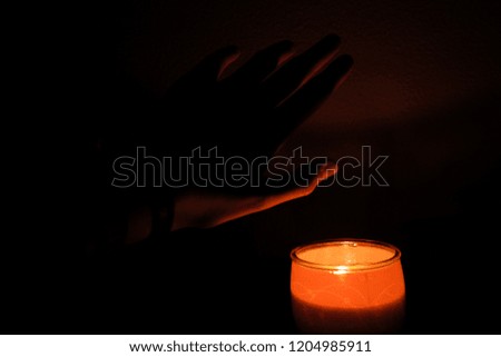 Picture of a candle and a hand. the whole picture is illuminated by the candle as the light reflects on the hand. everything is red 