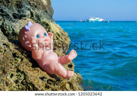The doll sits on the rocks of the sea
