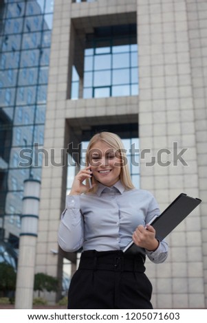 Woman using phone and holding documents.