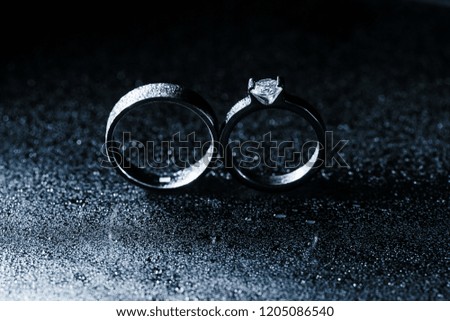 Classic white gold wedding and engagement rings close-up on wet sparkling background. Monochrome copy space photo.