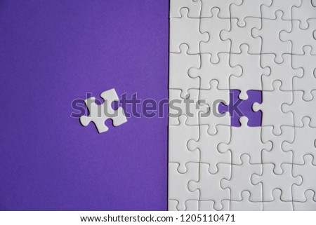 Missing jigsaw puzzle pieces. Business concept. Fragment of a folded white jigsaw puzzle and a pile of uncombed puzzle elements against the background of a Violet surface. Royalty-Free Stock Photo #1205110471