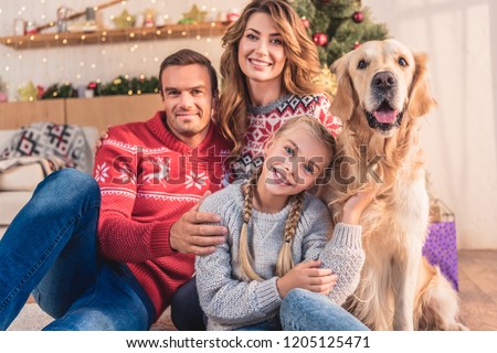 smiling family with golden retriever dog sitting near christmas tree with gifts