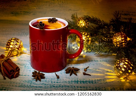 Hot mulled wine with orange, anise and cinnamon on the background of Christmas tree branches and garland. Warming Christmas drink. Festive mood.