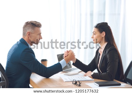 side view of businesspeople arm wrestling at workplace in office