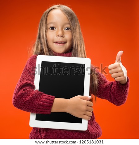 Little funny girl with tablet on studio background. She showing something and pointing at screen.
