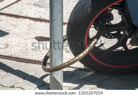 Rear wheel of powerful motorcycle locked with chain bike lock to road sign pole closeup in sunny day
