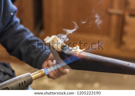 Expert carpenter burning a wood leg with a professional gas burner. Flames and smoke, fire and timber. Detailed shot of a professional laboratory, treating and processing wooden elements.