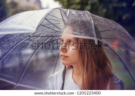 School-age girl under a transparent umbrella in the rain.