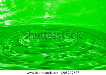 The droplet has a green background, dripping in the middle, causing a wave of water.